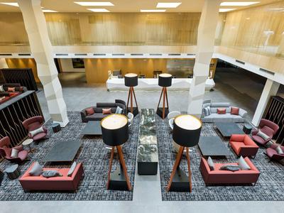 Moderní hotelová lobby s posezením, stojacími lampami a mramorovým pultem v otevřeném prostoru.