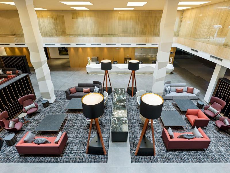 Area moderna della hall dell'hotel con gruppi di sedute, lampade da terra e bancone in marmo.