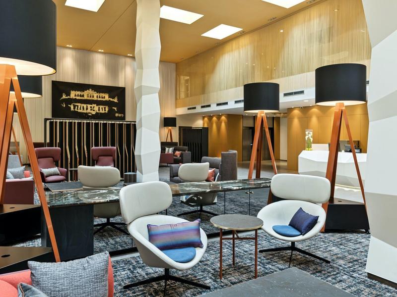 Lounge d'hotel moderna con sedie bianche, lampade da terra a treppiede e rivestimenti in legno.