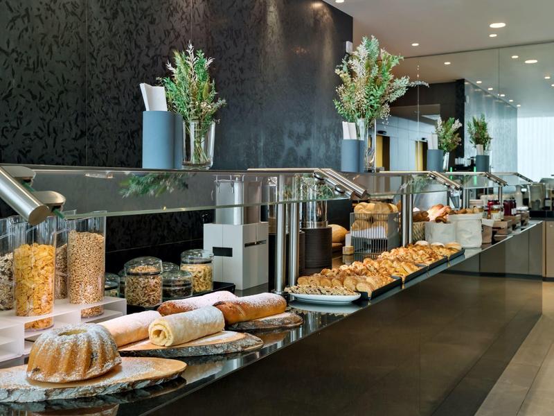 Elegante buffet per la colazione con pane, pasticcini, cereali e fiori freschi in un ambiente moderno.