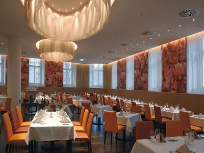 Salle à manger élégante avec tables dressées, chaises orange et éclairage élégant.
