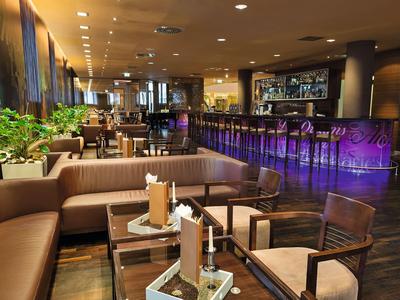 Bar d'hôtel moderne avec canapés en cuir, tables en bois et comptoir éclairé en couleurs.