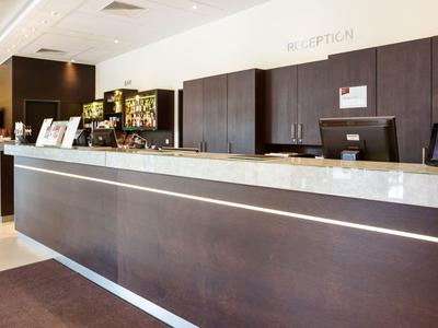 Moderner Rezeptionsbereich mit dunklem Holz, heller Arbeitsfläche und grünen Stühlen im Hintergrund.