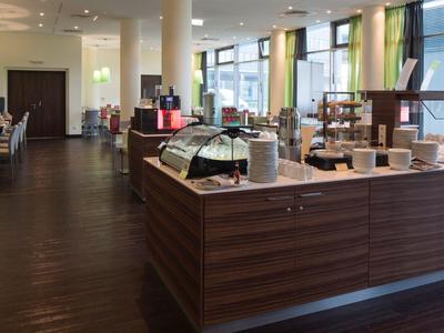 Café moderno de hotel con suelo de madera oscura y mostrador bajo grandes ventanales.