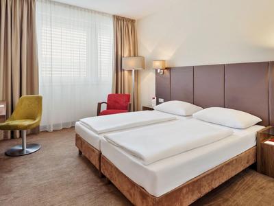 Moderna habitación de hotel con dos camas, escritorio, silla y ventana grande.