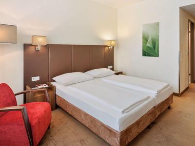 Habitación de hotel moderna con cama doble, sillón rojo y luces cálidas.