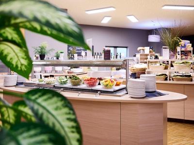 Bufet s čerstvým ovocem, pečivem a nádobím v světlé jídelně.