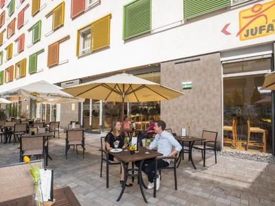 People sitting at tables under umbrellas in front of a modern hotel building.