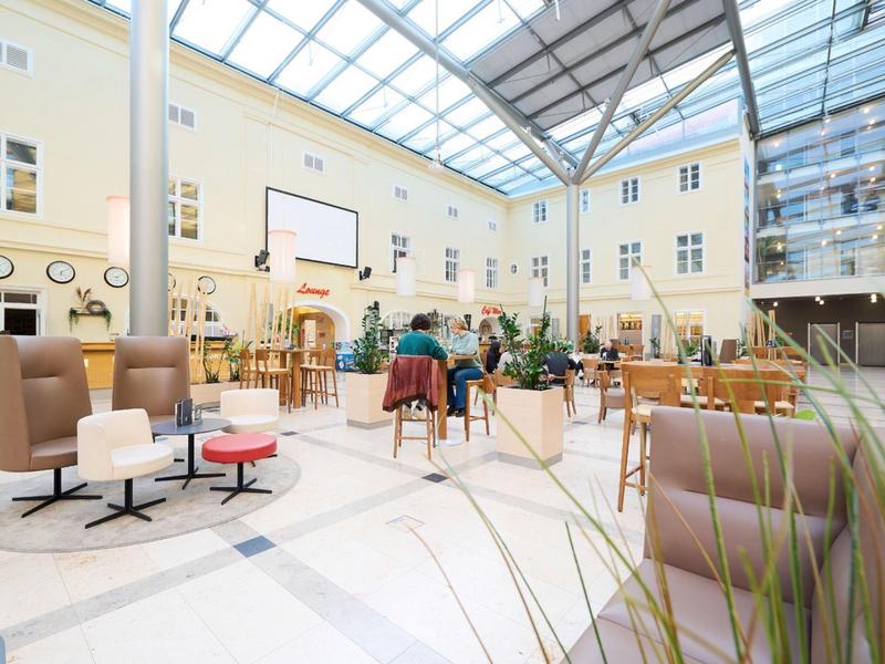 Světlý hotelový lobby s moderním posezením a skleněnou střechou