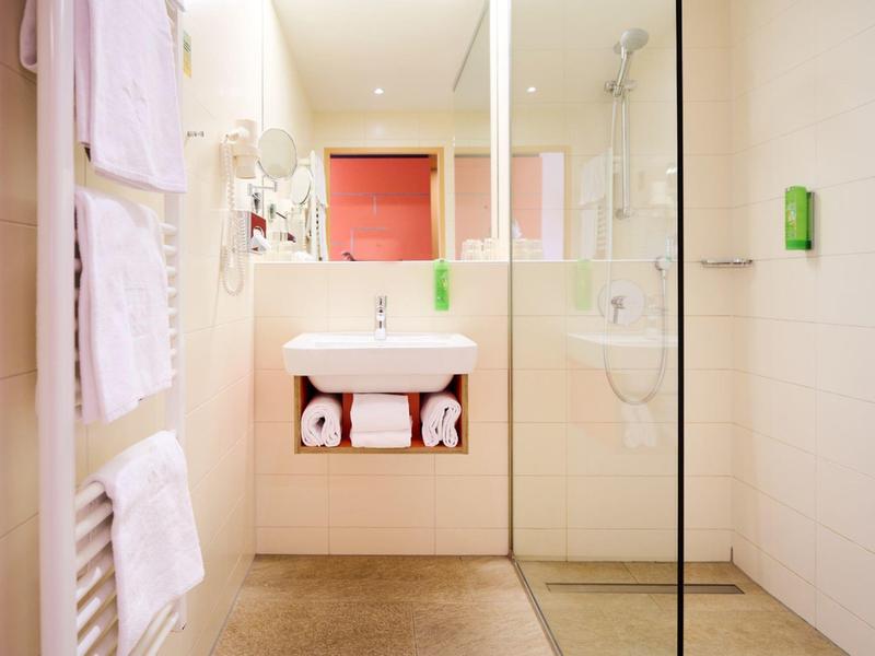 Světlá moderní koupelna se umyvadlem, ručníky a skleněným sprchovým koutem.