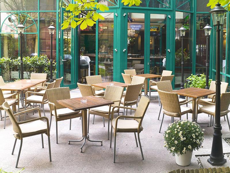 Leeg buitenterras van een café met bruine tafels, stoelen en groene gevel op de achtergrond