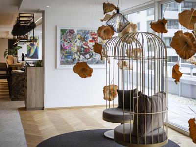 Nowoczesne lobby hotelowe z drewnianymi huśtawkami w formie klatki dla ptaków i wiszącymi dekoracjami z jesiennych liści.