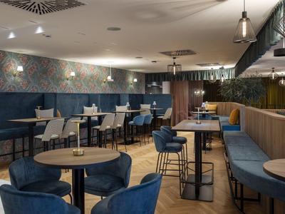 Nowoczesny salon hotelowy z niebieskimi fotelami, stolikami i przytłumionym oświetleniem.