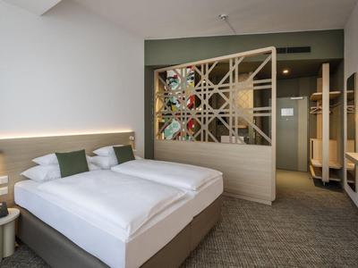 Nowoczesny pokój hotelowy z łóżkiem podwójnym, poduszkami dekoracyjnymi i ozdobną przegrodą w tle.