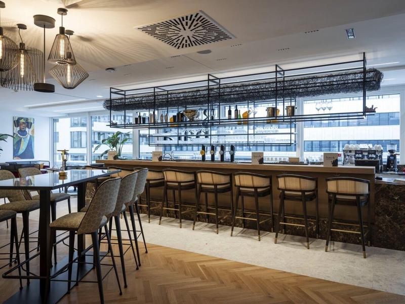 Nowoczesny bar hotelowy z wysokimi stołkami, stolikami i stylowym oświetleniem.