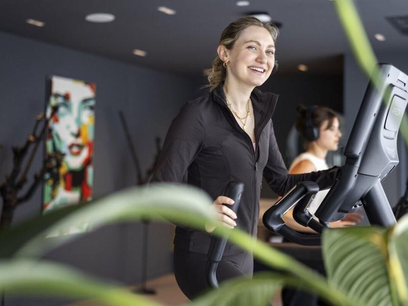 Młoda kobieta szczęśliwie ćwicząca na bieżni w nowoczesnej siłowni.