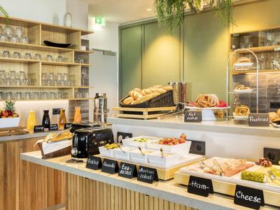 Buffet with a selection of breakfast items like bread, cold cuts, and cheese in a bright room.