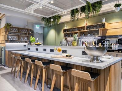 Modern breakfast area with long counter, wooden stools, and hanging plants under warm lighting.