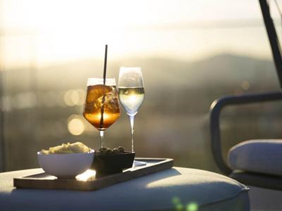 Zwei Getränke, ein Aperitif und ein Glas Wein, auf einem weißen Tisch mit Snacks bei Sonnenuntergang.