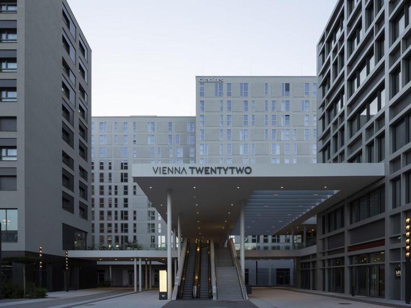 Modernes graues Bürogebäude mit breitem Eingang und Aufschrift "Vienna TwentyTwo" bei klarem Himmel.