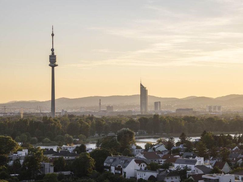 Stadtansicht mit Fernsehturm und Hochhaus vor einem sanft orangefarbenen Himmel bei Sonnenuntergang.