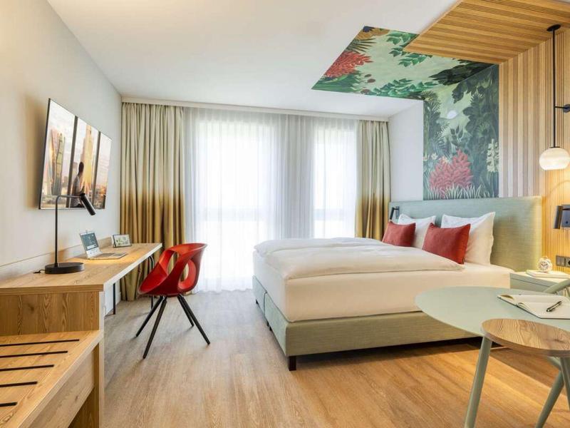 Modern eingerichtetes Hotelzimmer mit Doppelbett, Schreibtisch, Stuhl und blumiger Wanddekoration.