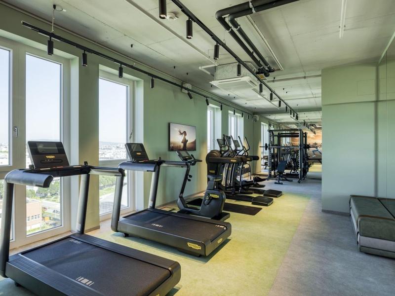 Moderner Fitnessraum mit Laufbändern, Crosstrainern, großem Fenster und heller Innenausstattung.