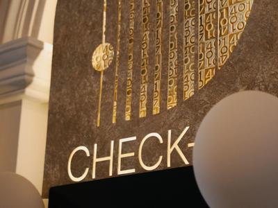 Detailansicht eines eleganten Check-in-Bereichs mit goldener Verzierung und Kioskbilschirm.