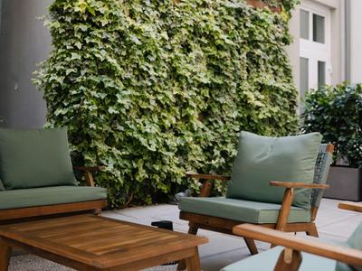 Terrasse confortable avec fauteuils verts, table en bois et grand parasol devant un mur recouvert de lierre.