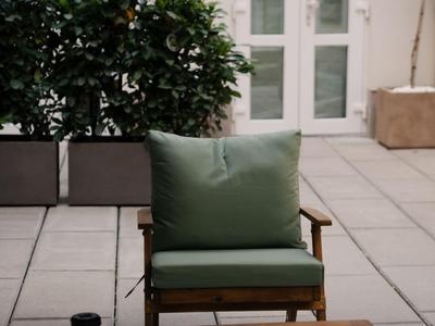 Une chaise verte avec coussin devant une porte blanche avec une table en bois sur une terrasse.