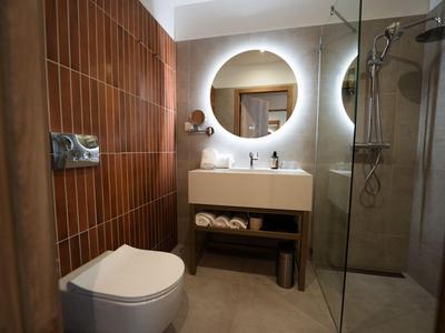 Salle de bain moderne avec lavabo suspendu, miroir rond et douche avec porte en verre.