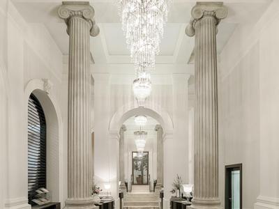 Elegancki hotelowy korytarz z wysokimi kolumnami, żyrandolami i marmurową podłogą w jasnym wystroju.