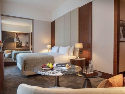 Modernes Hotelzimmer mit zwei Betten, Tisch, Sesseln und stilvoller Beleuchtung.