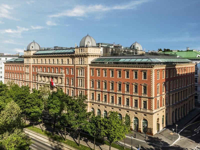 Großes historisches Hotelgebäude aus Backstein mit Bäumen davor unter blauem Himmel.