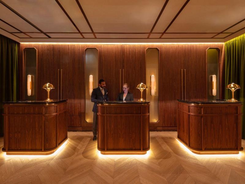 Eleganter Hotelempfang mit dunklem Holz, warmem Licht und zwei Personen am Empfangstresen.