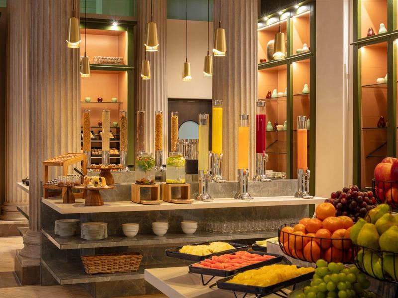 Luxuriöser Frühstücksbereich mit Buffet, modernen Pendelleuchten und Säulen in warmem Licht.