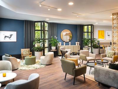 Salon d'hôtel moderne avec fauteuils confortables, canapés et plantes.