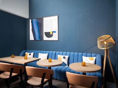 Coin salon confortable avec banquette bleue, tables et chaises devant un mur bleu.