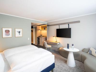 Chambre d'hôtel moderne avec un grand lit, canapé, table et télévision murale.