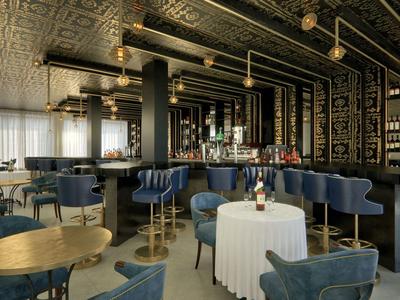 Elegante Hotelbar mit blauen Sesseln, goldenen Leuchten und schwarzer Wanddekoration.