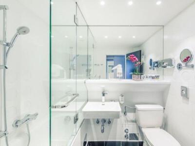 Helles, modernes Badezimmer mit weißer Keramik und Glasdusche in einem Hotelzimmer.