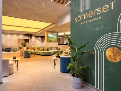 Moderner Hotel-Loungebereich mit grünen Akzenten, Sitzgelegenheiten und Pflanzen.