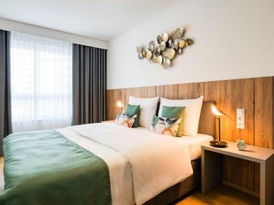 Helles Hotelzimmer mit großem Bett, Holzverkleidung, Kunst an der Wand und Nachttischlampe.