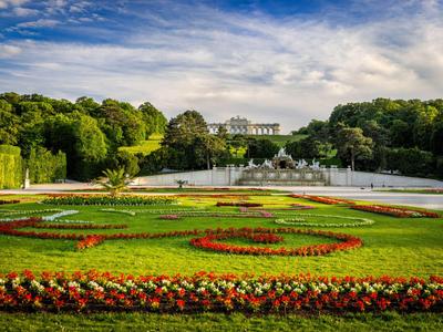 Ein gepflegter Garten mit bunten Blumen und Büschen vor einem weißen Gebäude und blauem Himmel.