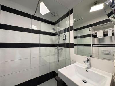 Bagno moderno con doccia e lavabo, piastrelle bianche e nere a strisce.