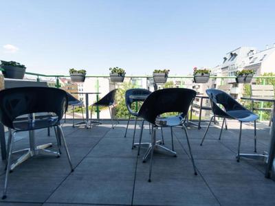 Sedie nere vuote e tavoli su una terrazza soleggiata di un hotel con vista su edifici.