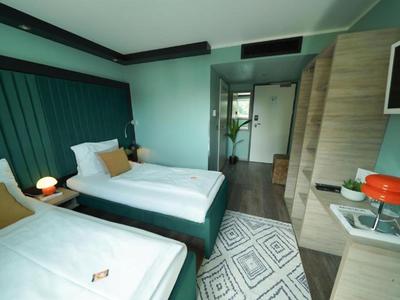 Camera d'hotel moderna con due letti singoli, moquette e scrivania con televisore.