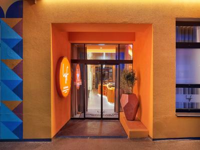 Entrée d'un hôtel avec murs orange, porte vitrée et banc décoratif.