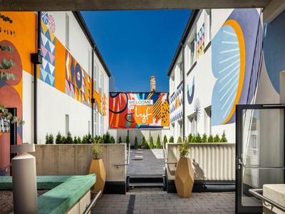 Cour d'hôtel moderne avec des fresques colorées, des marches et des sièges sous un ciel clair.