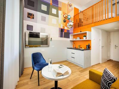 Chambre d'hôtel moderne avec mezzanine, coin salon et cuisine compacte aux tons chauds.